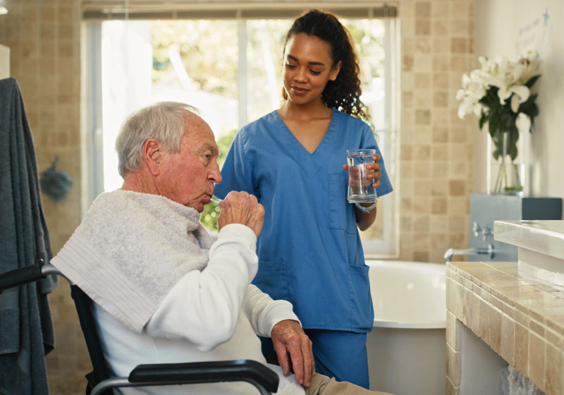 Care working helping an senior man brush his teeth