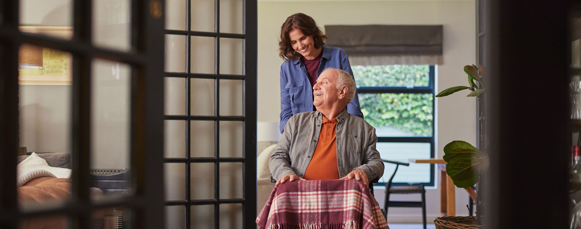 Care provider pushing a senior man in a wheel chair and speaking happily to one another
